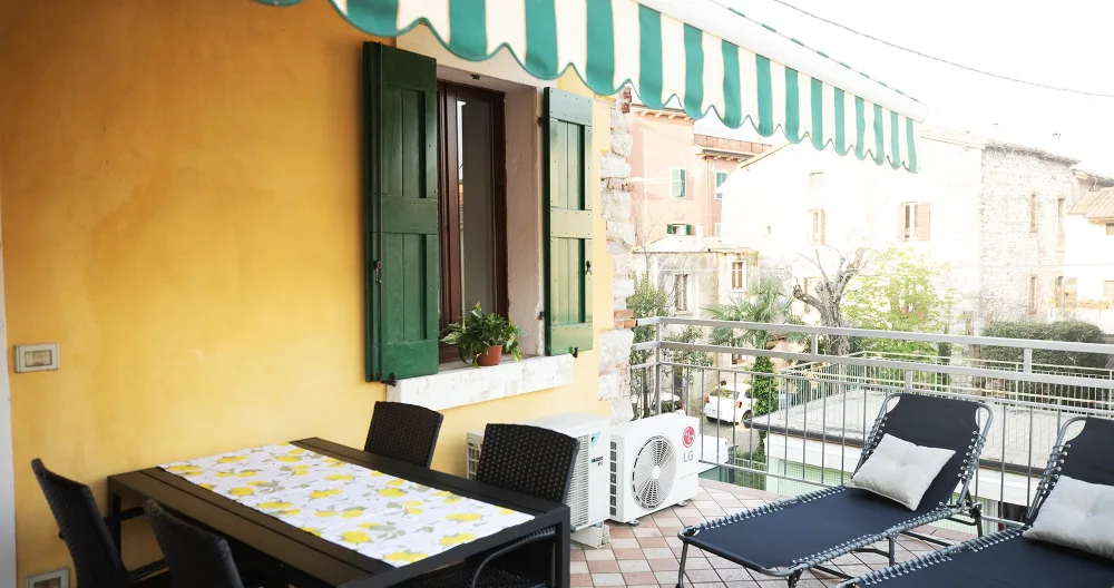 FRANCESCA's listing on misterb&b - Terrazza con tenda elettrica, tavolo con 4 sedie e 2 sdraio dove godere del caldo e sole respirando l'aria fresca del lago di Garda a pochi metri di distranza.