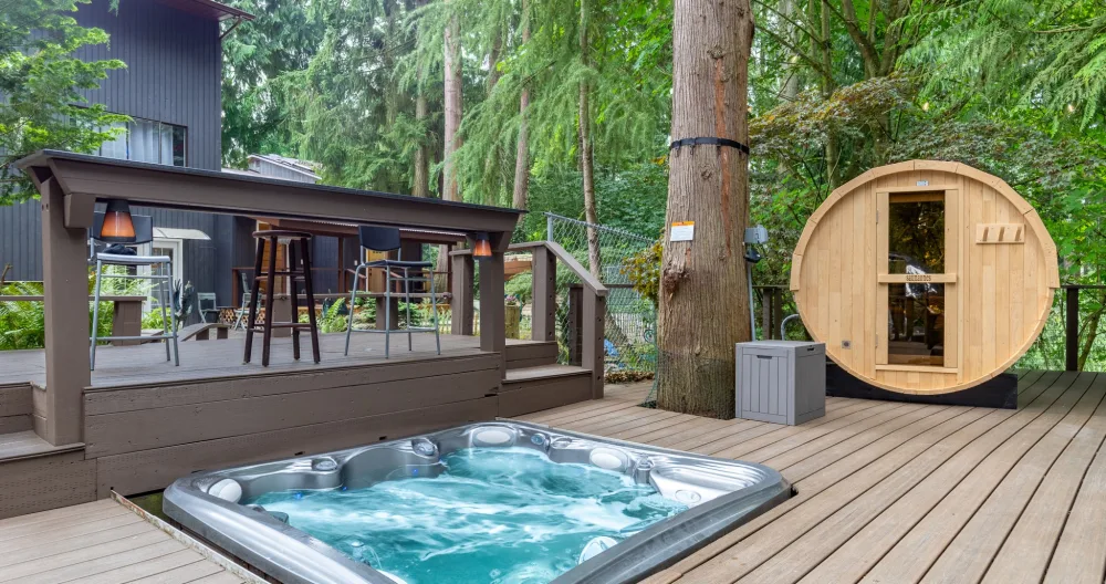 Jackies Inserat auf misterb&b - The hot tub sits just beneath the deck, right next to the sauna, surrounded by tall trees for a serene and private setting.