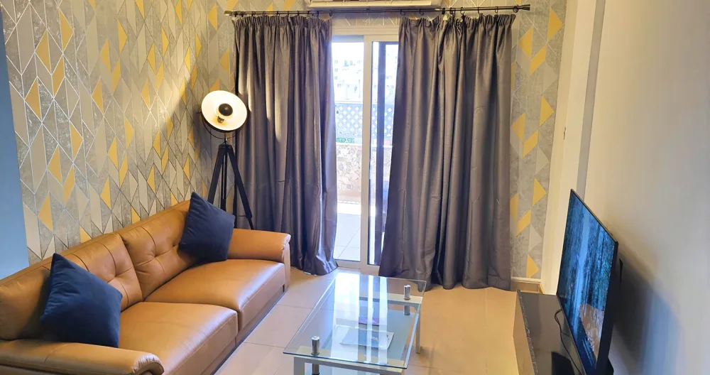 Anuncio de Marinos en misterb&b - Modern & cozy living room! Plush brown leather sofa, huge smart TV, chic yellow-grey geometric walls, glass coffee table, AC + balcony access. Relax in style
